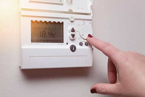 Un doigt règle le thermostat du chauffage électrique sur 18°4